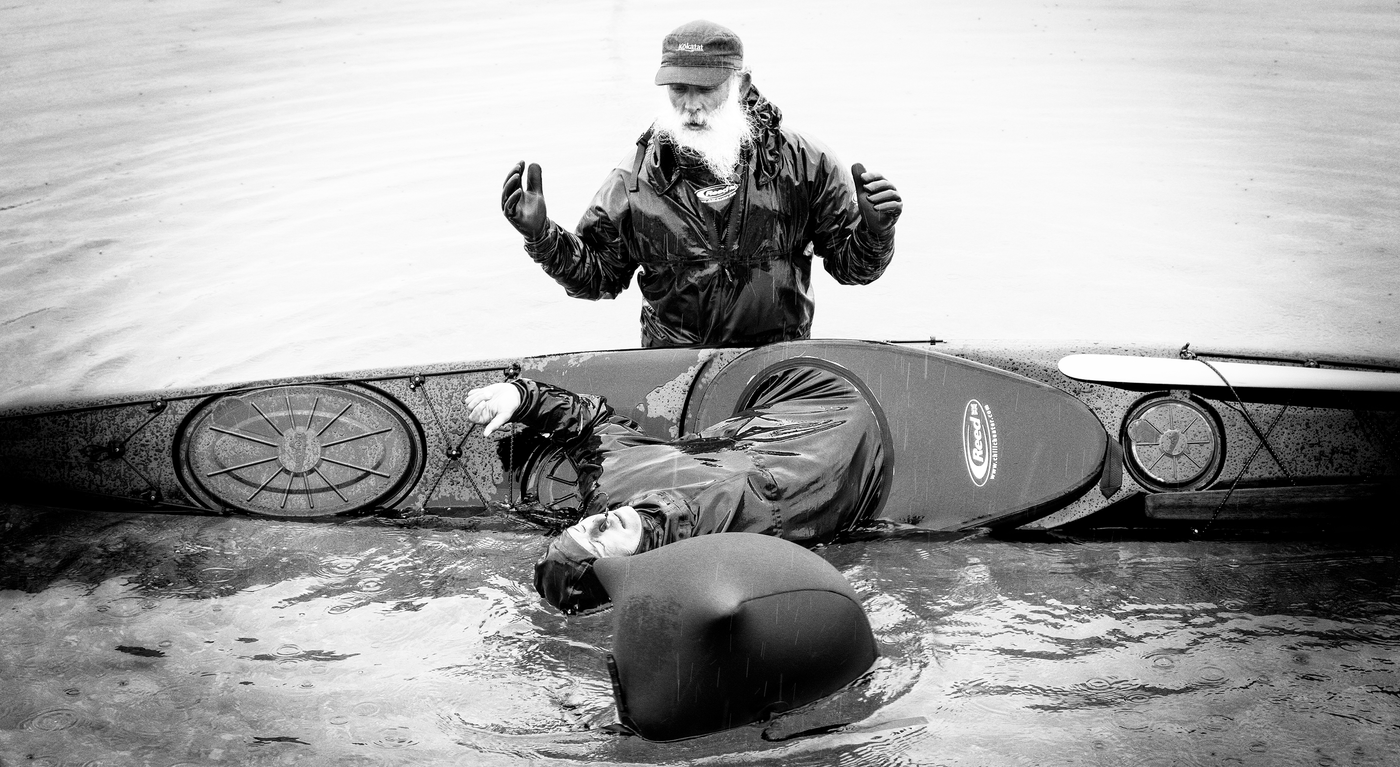 Bearded man waist deep in the water helping a lady in a kayak to roll upright. Black and white image