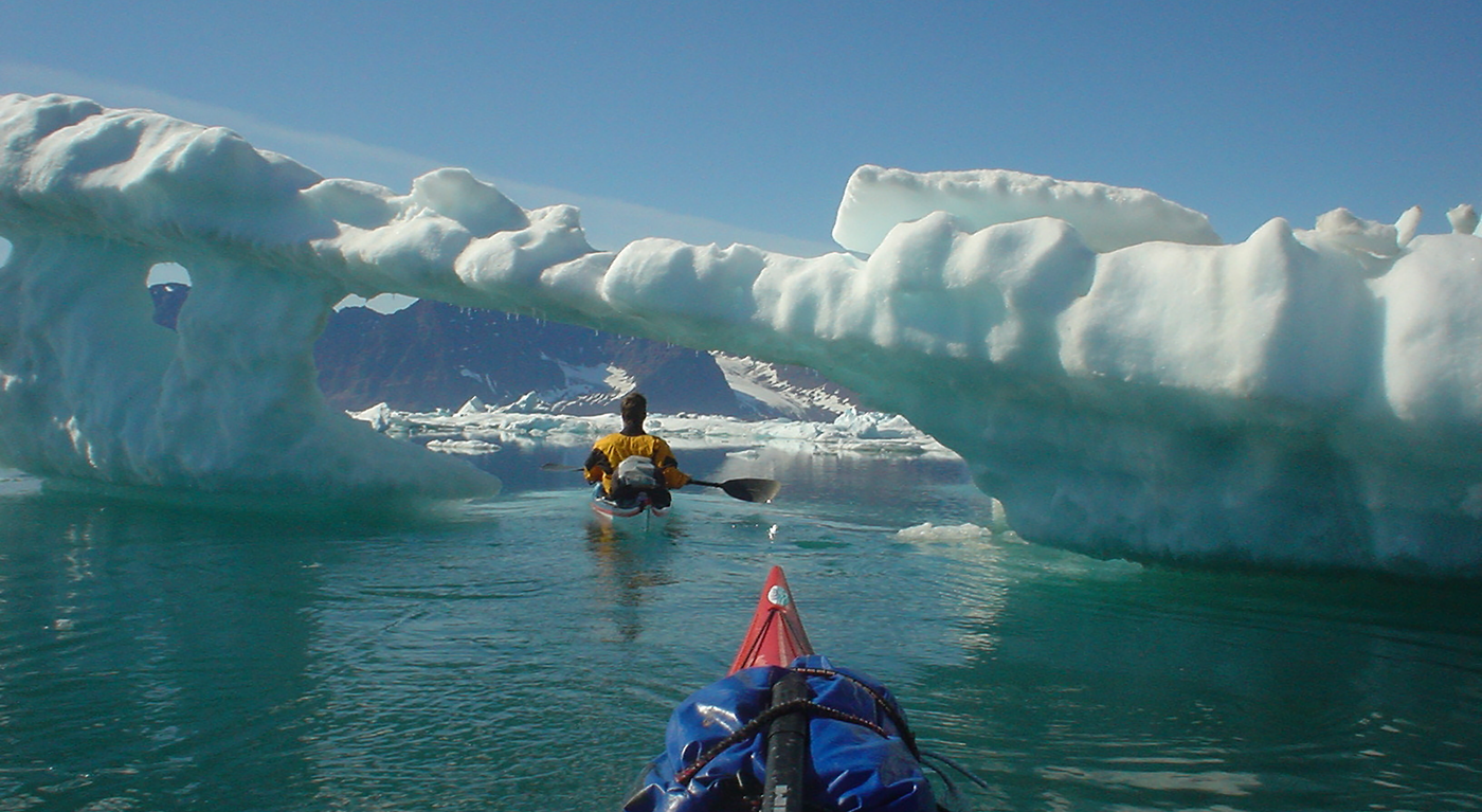 two kayakers paddling under ice bridge in Greenland